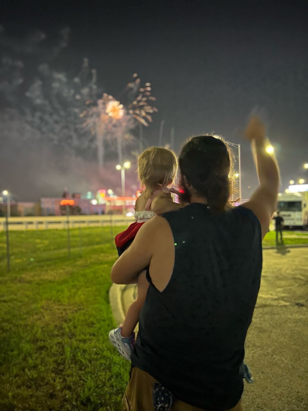 Bond Henry, seen from behind, holding his young daughter and waving at fireworks at night